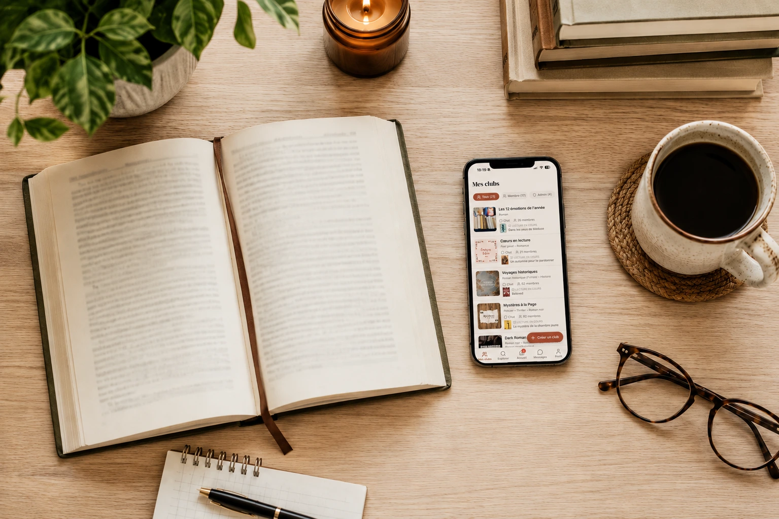 Livre ouvert et smartphone affichant Booklub sur un bureau cosy, avec café, bougie et accessoires de lecture.
